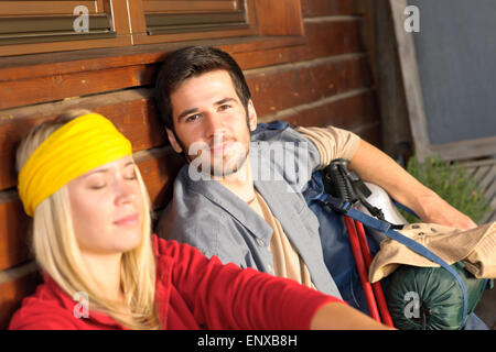 Tramping young couple backpack relax by cottage Stock Photo