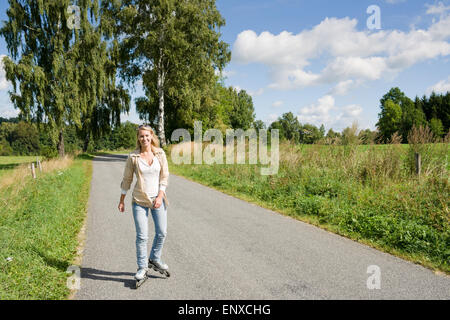 Inline skating young woman on sunny asphalt road Stock Photo