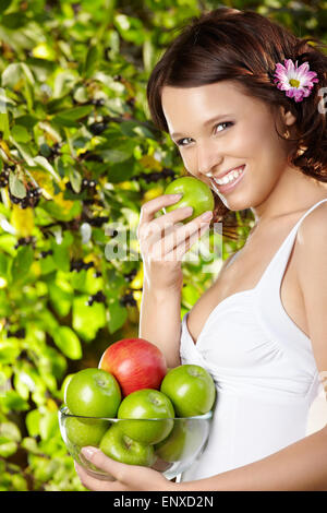 Girl eats an apple with bowl of apples in a summer garden Stock Photo