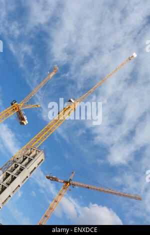 Yellow tower cranes against a blue sky with broken cloud formation Stock Photo