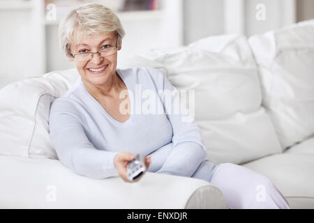 Mature woman TV remote control changes channels Stock Photo