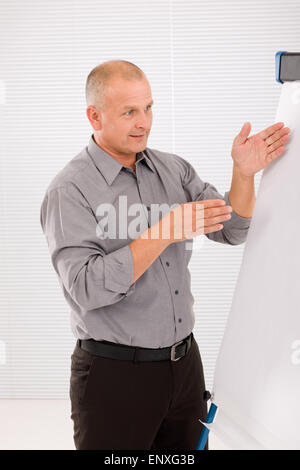 Mature businessman pointing at empty flip chart Stock Photo