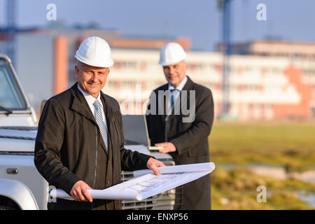 Two architects at construction site review plans Stock Photo
