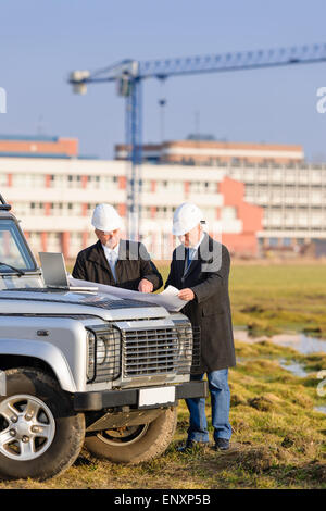 Two architects at  construction site review plans Stock Photo