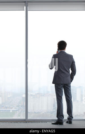 businessman with mobile phone looking through window Stock Photo
