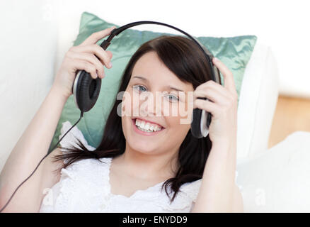 Jolly woman putting headphones lying on a sofa Stock Photo