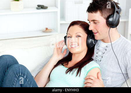 Charming couple listening to music with headphones lying on the sofa Stock Photo