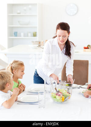adorable mother serving salad to her children for lunch Stock Photo