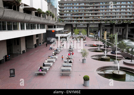 People sitting outside at tables on the lakeside terrace piazza of the Barbican Centre exterior and lakeside lake terrace with a view of Barbican Estate flats in spring London EC2Y England UK  KATHY DEWITT Stock Photo