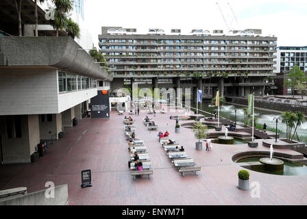 People sitting outside at tables on the forecourt of the Barbican Centre terrace exterior and lakeside lake terrace with a view of Barbican Estate flats in spring London EC2Y England UK  KATHY DEWITT Stock Photo