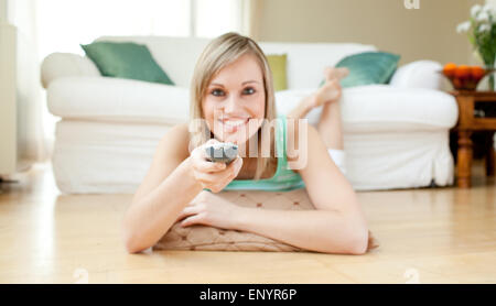 Blond young woman watching TV lying on the floor Stock Photo