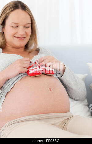 Happy future mom putting baby shoes on her belly Stock Photo