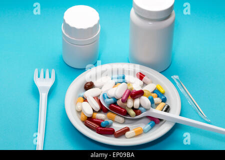 Different pills on a plate with two bottle,spoon and fork on a blue background Stock Photo