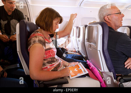 A woman passenger on a plane using an iPad, sitting in her seat in the cabin, in flight, Monarch Airlines flight Stock Photo