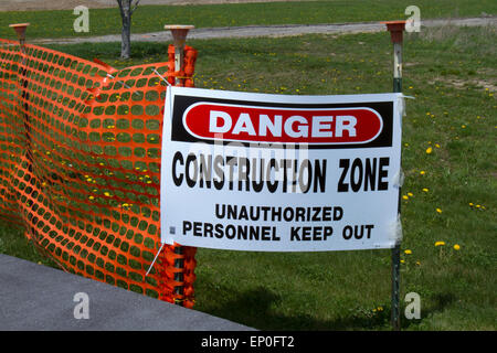 Sign reading Danger, Construction Zone, Unauthorized Personnel Keep Out along sidewalk with orange safety netting. Stock Photo