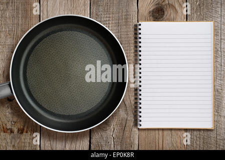 Frying pan and recipe book on wooden background Stock Photo