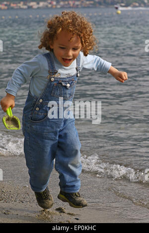 Little boy jumping and playing with sand on a beach by the lake Stock Photo