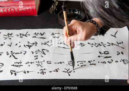 Man's hand using a brush to paint Chinese calligraphy on a large sheet of white paper in Gaithersburg, Maryland. Stock Photo