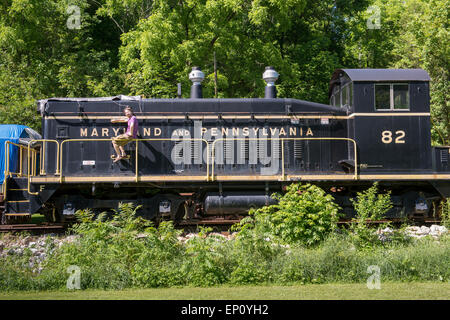 Young man sitting on railing next to historic train in Muddy Creek Forks, Pennsylvania, USA Stock Photo
