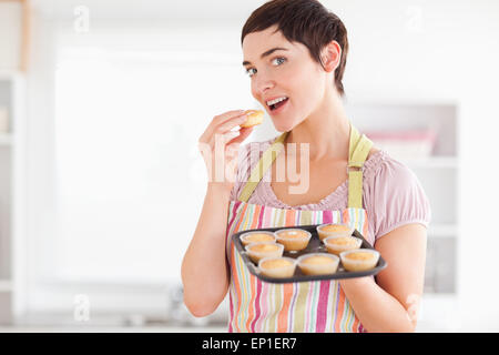 Joyful brunette woman showing muffins while eating one Stock Photo