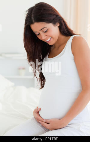 Portrait of a beautiful pregnant woman touching her belly while sitting on a bed Stock Photo
