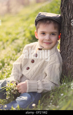 Boy leaning against a tree trunk, holding bunch of spring flowers Stock Photo