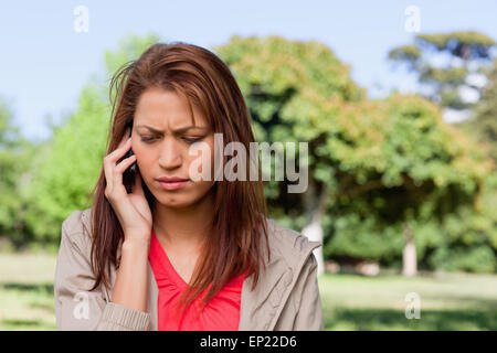 Woman looking towards the ground while on the phone in a bright grassland area Stock Photo