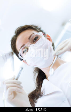 Dentist wearing surgical mask while holding angled mirror and drill, ready to begin Stock Photo