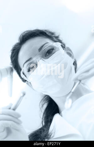 Dentist wearing surgical mask while holding angled mirror and drill, ready to begin Stock Photo