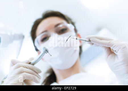 Dentist wearing surgical mask while holding angled mirror and drill, ready to begin Stock Photo