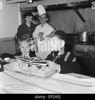 Mrs Sterry and her two children visit Mr Sterry, who works as an assistant crew cook on the 'Bloemfontain Castle' motor vessel. Mrs Sterry asked the Daily Mirror to photograph her husband with the ship in the background, as he was due to be transferred when the ship was sold to the Greeks. The Daily Mirror went one better and invited the family to visit the ship and toy fair at Kensington High Street. Picture shows Susie and Richard look at the model yacht that Mr Sterry brought them back from South Africa. Mr and Mrs Sterry watch in the background, 12th November 1959. Stock Photo