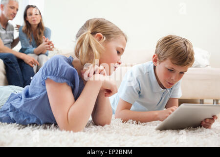 Siblings using a tablet computer with their parents on the backg Stock Photo