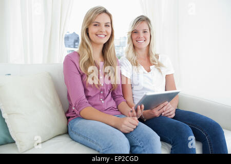 Two sisters looking at the camera as they hold a tablet pc in their hands Stock Photo