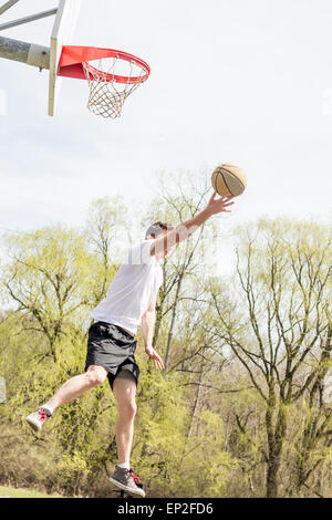 Young man doing basketball trick shots as he leaps through the air Stock Photo