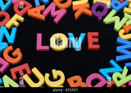 LOVE written in and framed by a scatter of colourful children's toy alphabet letters on a black background Stock Photo