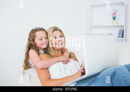 Daughter hugging mother whose working on laptop Stock Photo
