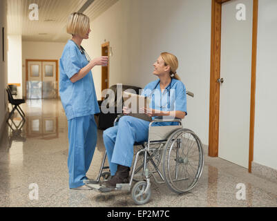 Nurse with drink talking to nurse in wheelchair with folder Stock Photo