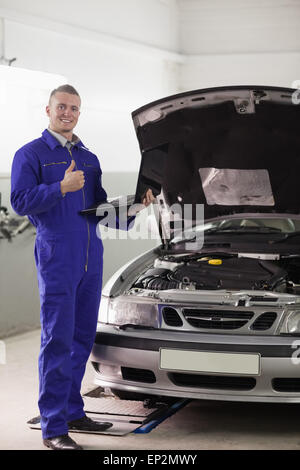 Smiling mechanic holding a computer with thumb up Stock Photo