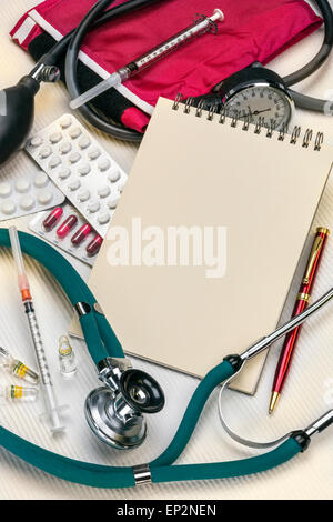 A doctors stethoscope and sphygmometer with syringes, drugs and a notepad - with space for text. Stock Photo