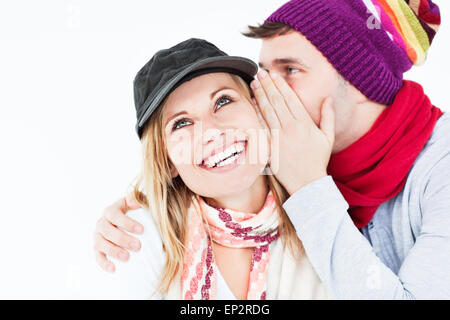 Handsome man with hat telling a secret to his laughing girlfriend against a white background Stock Photo