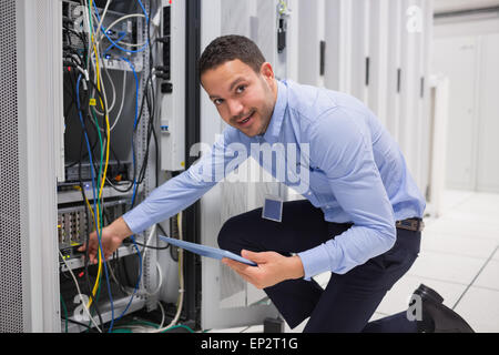 Smiling technician with tablet pc plugging cables into server Stock Photo