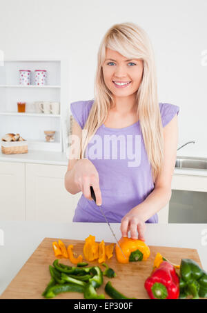 Beautiful blonde woman cutting peppers in modern kitchen interior Stock Photo
