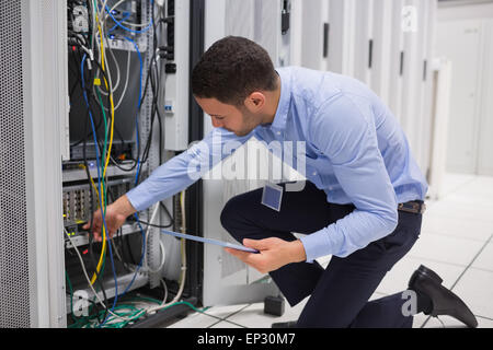 Man checking tablet pc as he is plugging cables into server Stock Photo