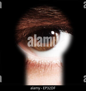 Scared male eye spying through a keyhole Stock Photo