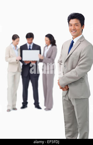 Smiling salesman with laptop and colleagues behind him Stock Photo - Alamy