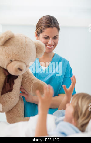 Smiling nurse showing a teddy bear to a child Stock Photo