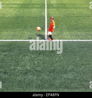 Side view of a boy kicking a ball on a football pitch Stock Photo