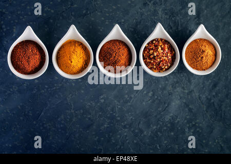 Different spices in tasting spoons on dark slate from above Stock Photo