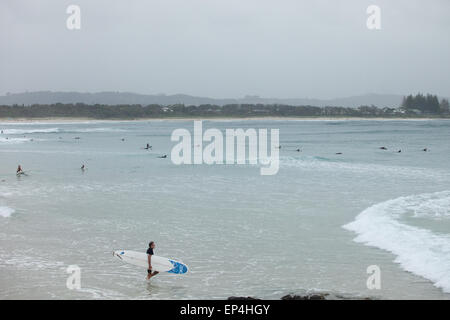 A surfer walks out to the pass as other surfers paddle out into the break in Byron Bay, Australia. Stock Photo