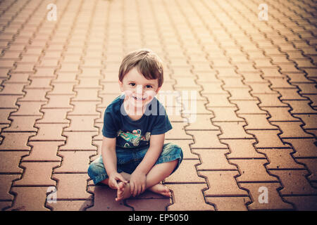 smiling little boy sitting on the ground Stock Photo